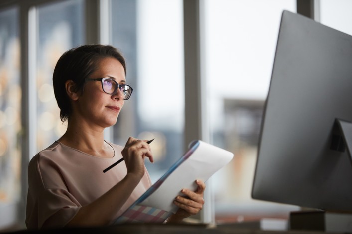 Woman taking notes while looking at her PC