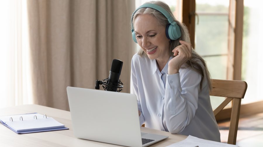 Woman wearing headphones and sitting in front of a laptop and microphone